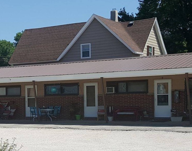 The Janco Motel building in Grand Junction, Iowa — a single-story brick motel with room doors opening onto the parking court and front lawn, seen on a summer day